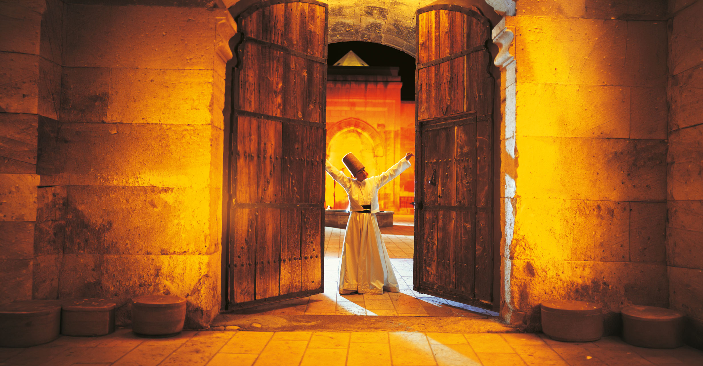 A whirling dervish at the Saruhan threshold — between the stone gate and the warm interior